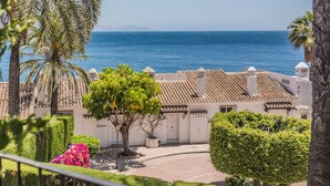 A coastal view with a clear sky, palm trees, and a building with a tiled roof. - APARTAMENTOS PUERTO MARINA DEL ESTE (Almunecar)