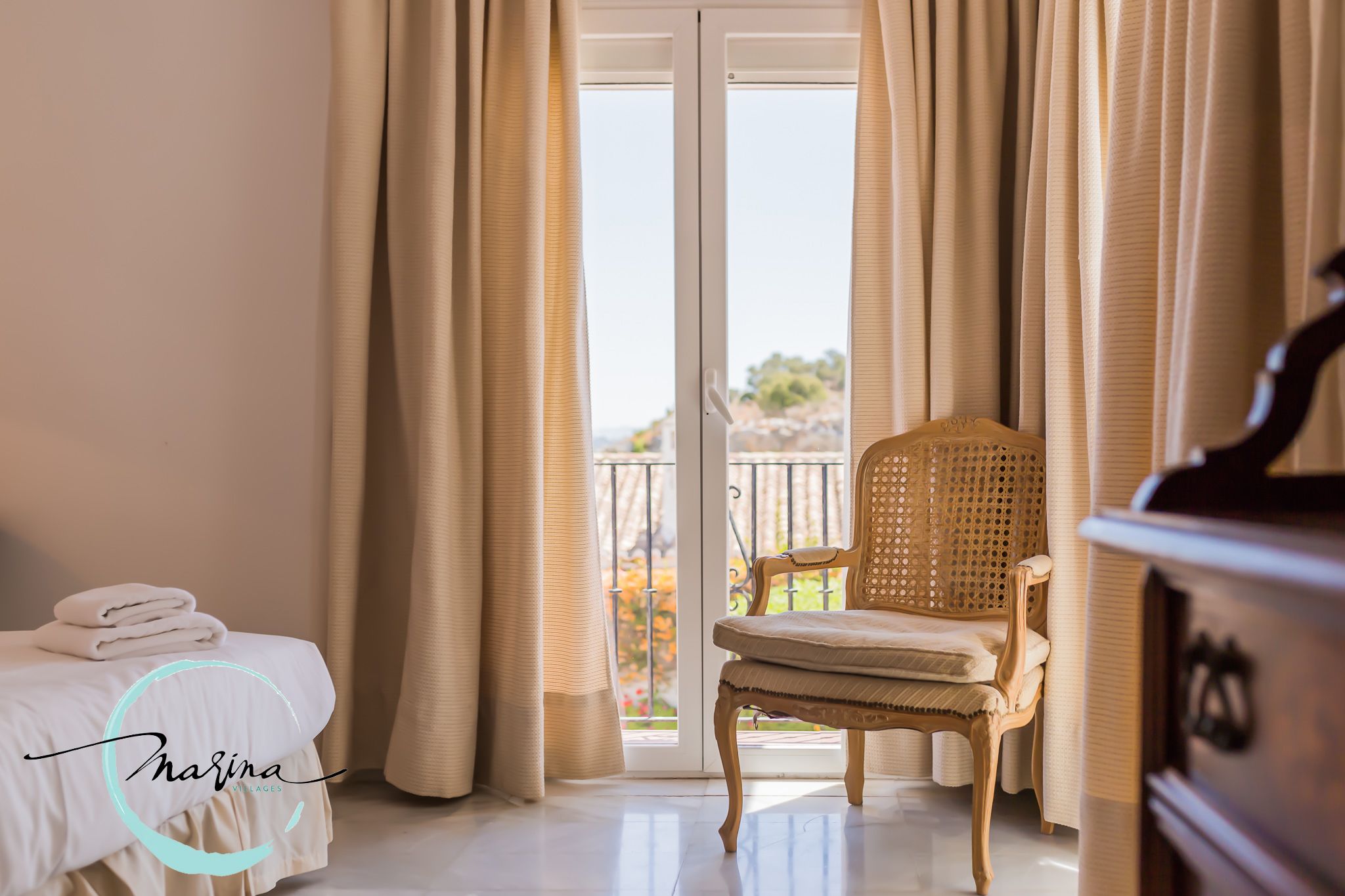Una habitación de hotel con cama, una silla, cómoda y balcón con cortinas.