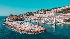 A coastal town with a marina, rocky breakwater, and a lighthouse. - APARTAMENTOS PUERTO MARINA DEL ESTE (Almunecar)