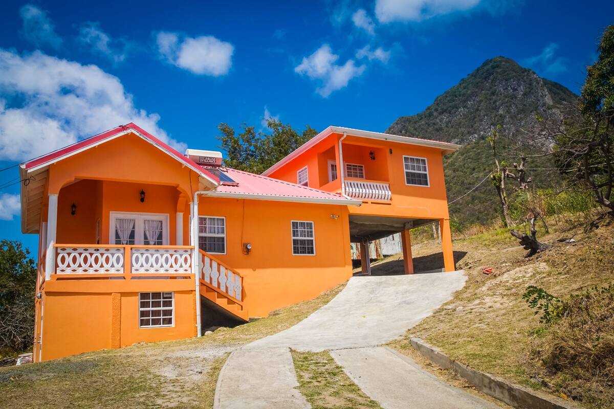 Una casa de dos pisos con techo rojo, barandillas blancas y un sendero de concreto que lleva a la entrada.