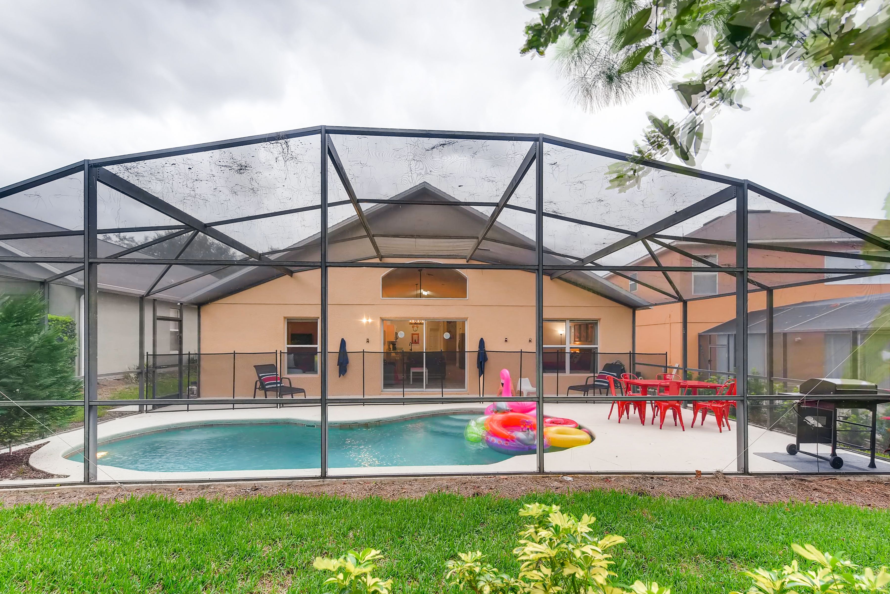 Une piscine extérieure couverte, protégée par une structure en verre, entourée de chaises rouges et d’un espace barbecue.