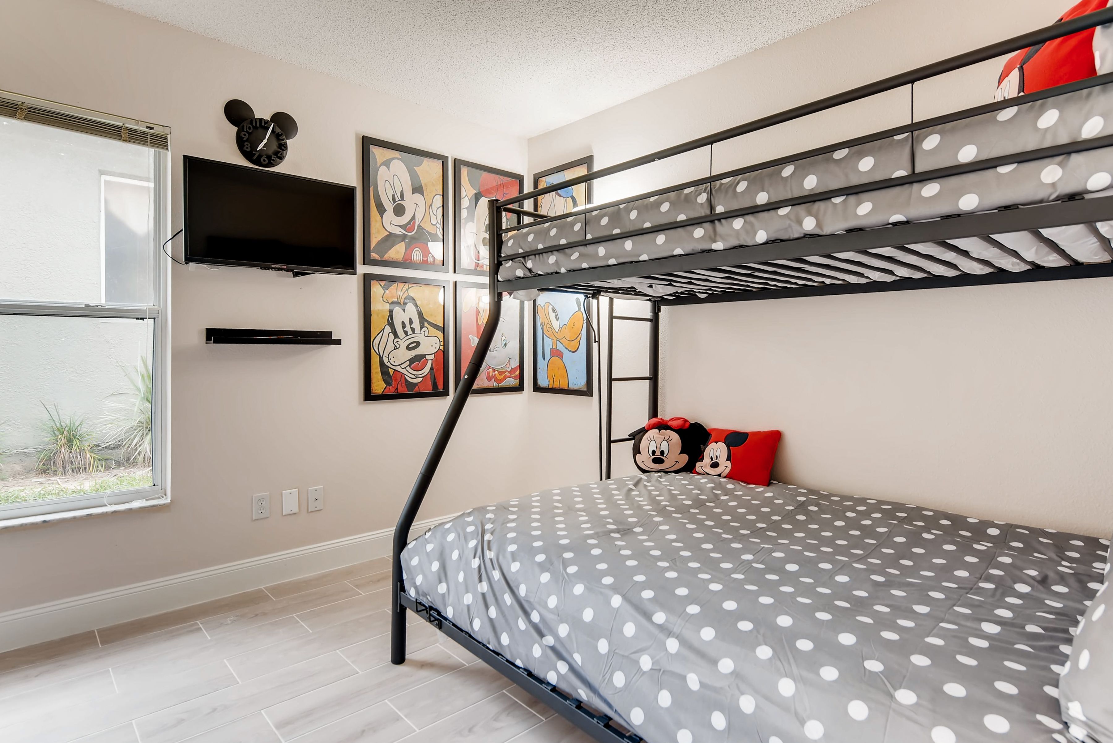 A bunk bed with a polka dot bedspread, a Mickey Mouse clock, and cartoon character posters on the wall.