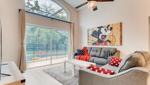 Una sala de estar con un sofá gris, una mesa de centro blanca y un ventanal con vistas a una piscina.