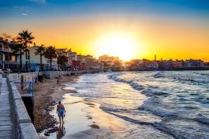 Una playa con atardecer, olas y edificios al fondo.