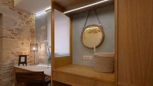 Een badkamer met een houten wastafelmeubel, een spiegel, een lijst met een afbeelding, een rieten mand en een stenen muur.