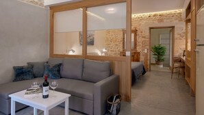 Een moderne woonkamer met een grijze bank, een klein wit tafeltje met een fles wijn en glazen, en een houten schuifdeur naar een slaapkamer.