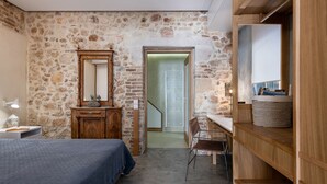 Een slaapkamer met een stenen muur, een houten dressoir, een bed, een bureau en een spiegel.