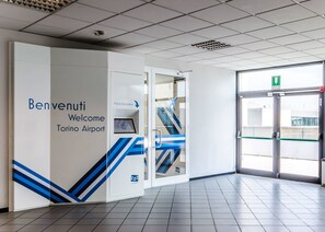 Una entrada moderna al aeropuerto con un letrero que dice 'Welcome', un área de recepción virtual y una vista despejada al exterior.