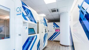 Un pasillo de hotel moderno con decoración azul y blanca, que incluye habitaciones numeradas y un quiosco digital.