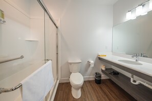 Casa de banho moderna com cabine de duche em vidro, sanita branca, lavatório com espelho e chão em madeira escura.