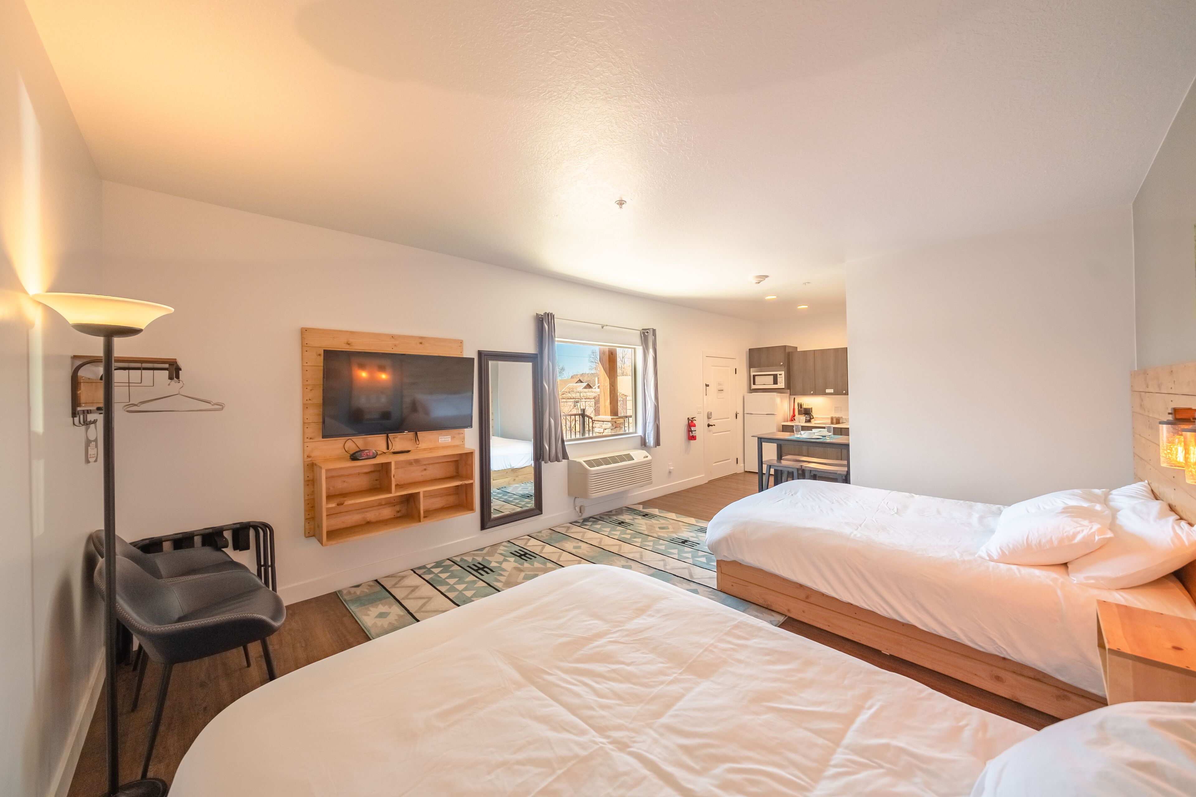 A hotel room with two beds, a TV, a desk, and a view of the outside.