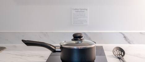 Een keuken met een moderne inductiekookplaat, een pan met deksel, en een spatel op een marmeren aanrecht.