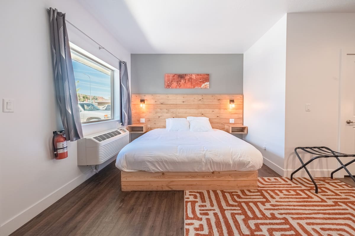 A bedroom with a wooden headboard, white bedding, a patterned rug, and a window with curtains.