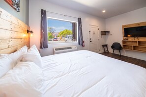 Quarto com uma cama grande, janela com cortinas, TV fixada na parede e um pequeno espaço de trabalho.
