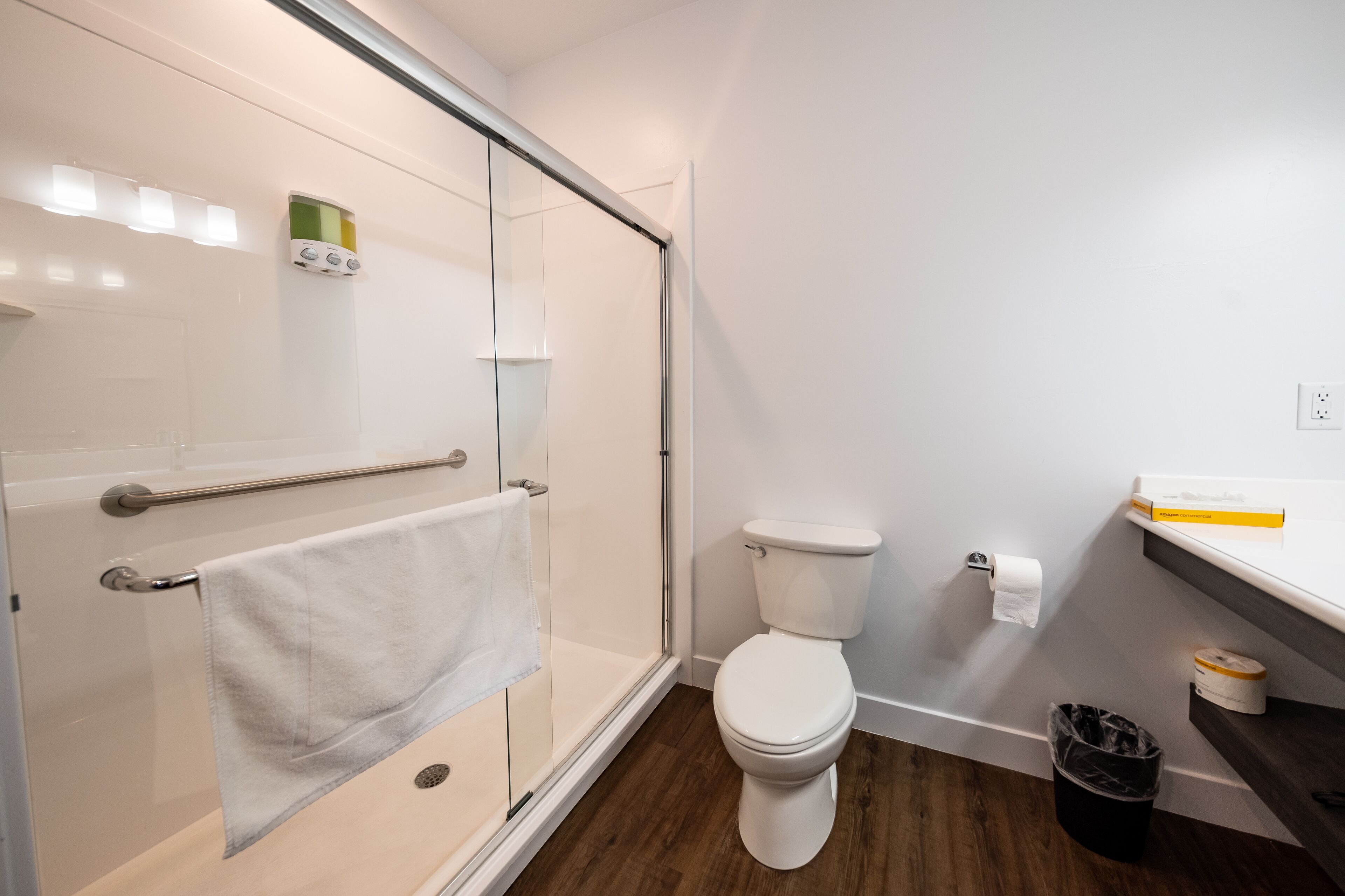 A modern bathroom with a glass shower enclosure, a white toilet, and a wooden floor.