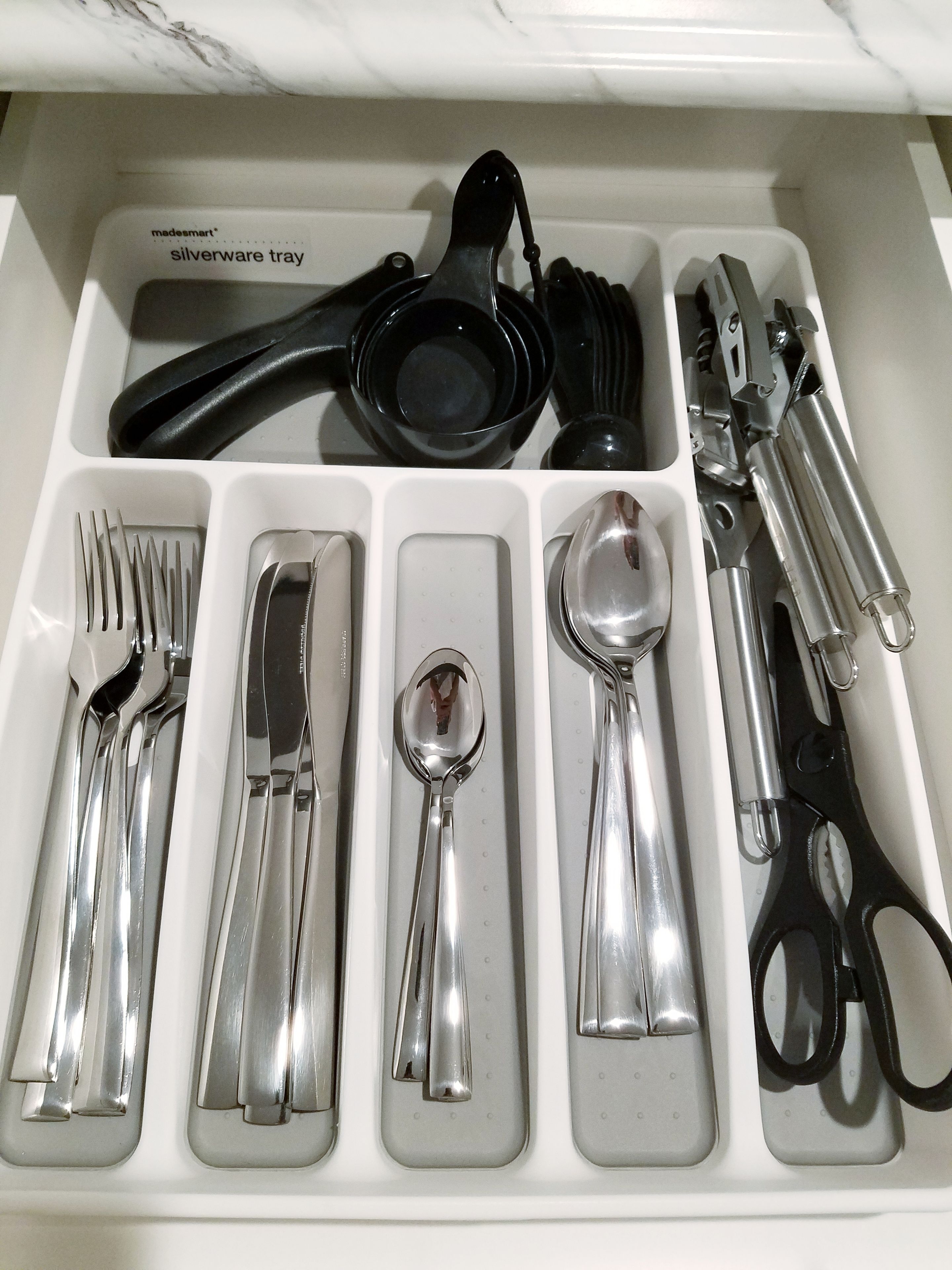 A drawer containing a silverware tray, forks, knives, spoons, and scissors.