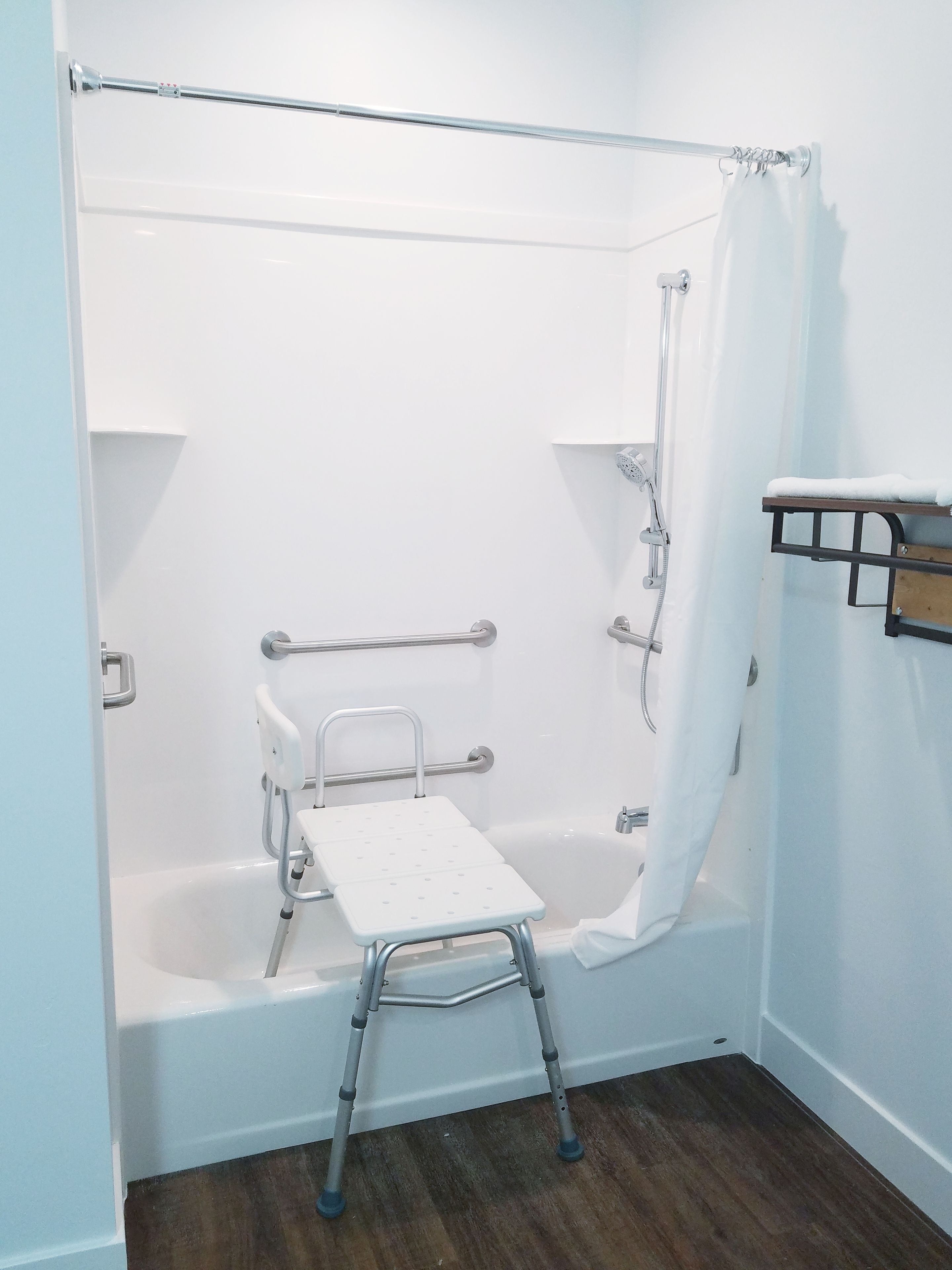 Ein Badezimmer mit einer weißen Badewanne, einem Duschvorhang, einer Haltestange, einer weißen Ablage und einem Holzregal.