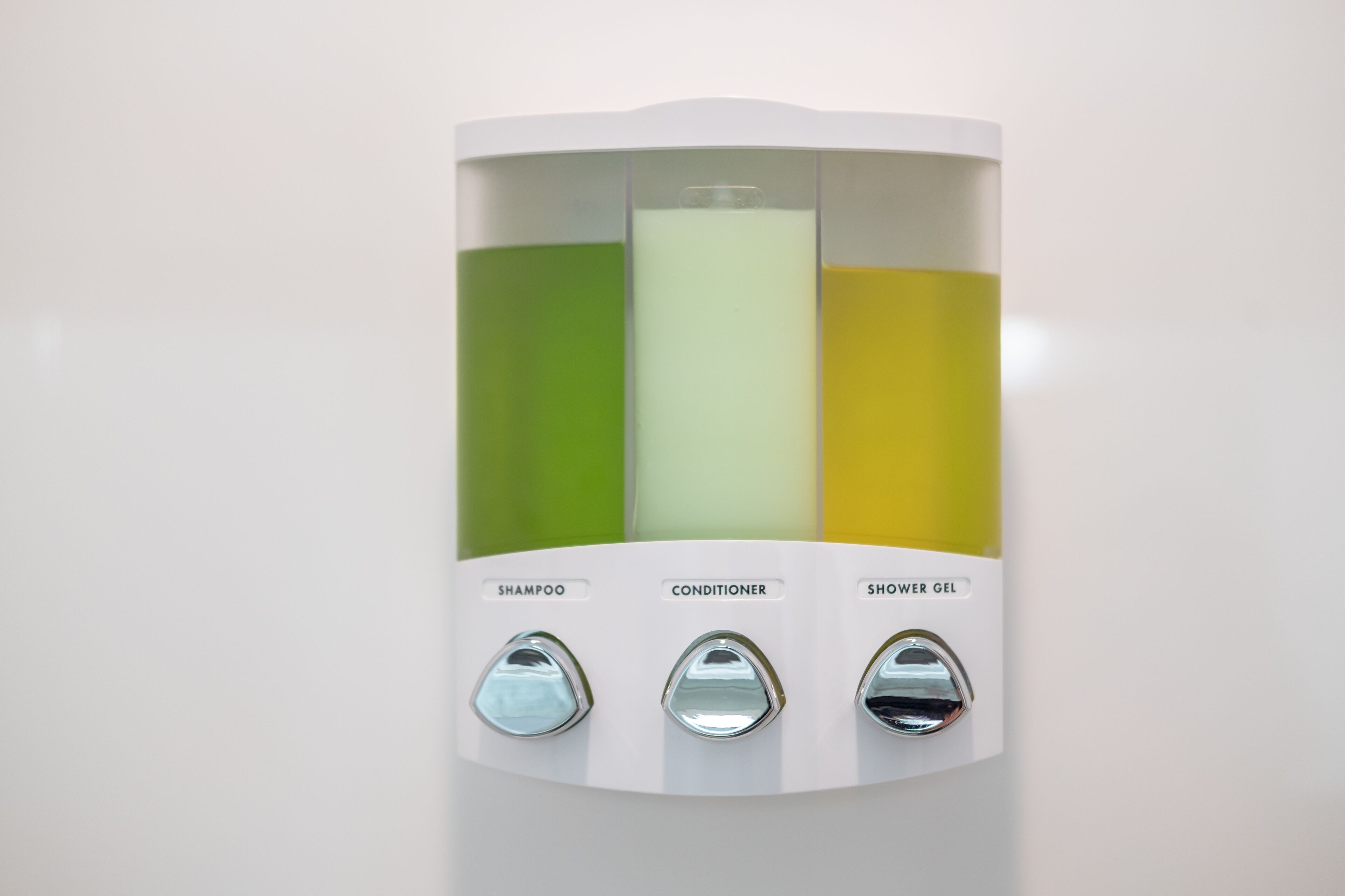 A wall-mounted dispenser with three compartments labeled for shampoo, conditioner, and shower gel.