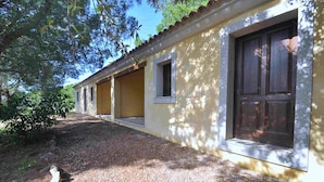 A building with a yellow exterior, a gravel pathway, and a wooden door. - Appartamenti in Gallura (Badesi)