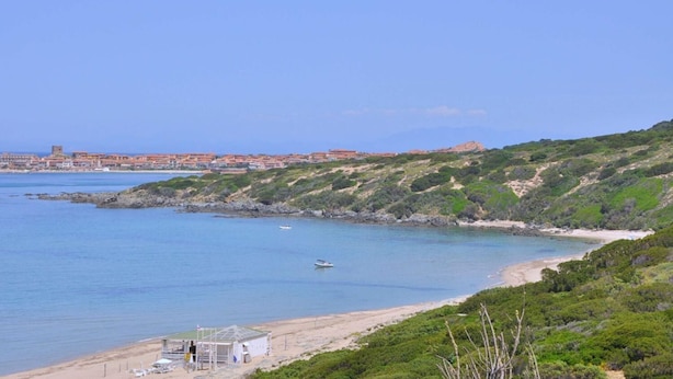 A coastal view with a beach, a small boat, and a distant town with buildings. - Appartamenti in Gallura (Badesi)