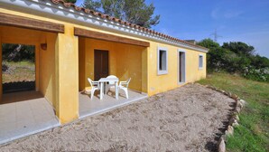 A yellow building with a tiled roof, a patio with a table and chairs, and a small window. - Appartamenti in Gallura (Badesi)