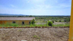 A view from a window overlooking a rural landscape with a building featuring a tiled roof and a stone wall in the foreground. - Appartamenti in Gallura (Badesi)