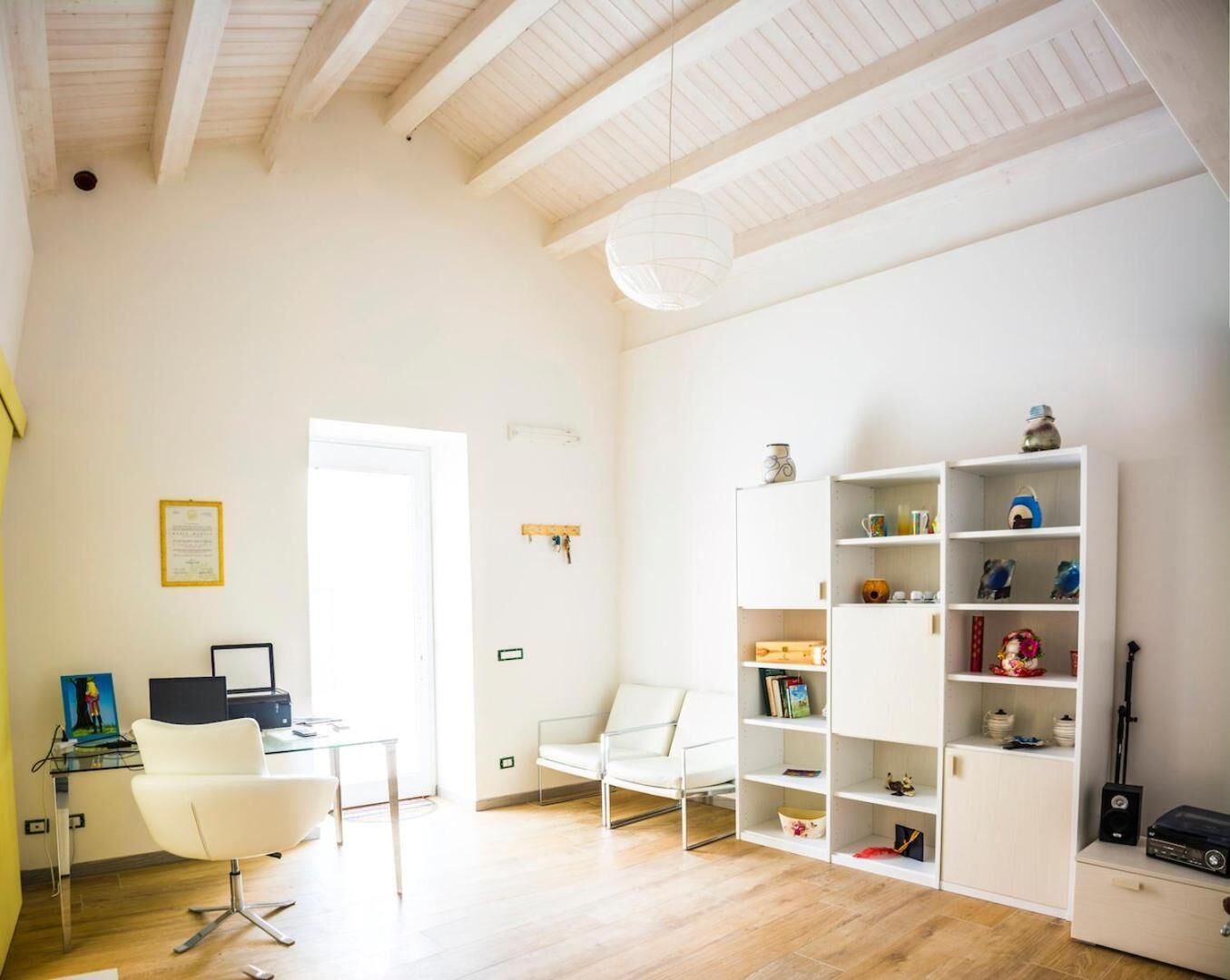 Un espacio habitable amplio y luminoso, con un sofá blanco, una mesa de vidrio, una estantería blanca y un techo de madera.