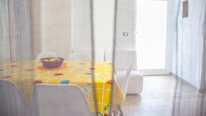 Un comedor con una mesa cubierta por un mantel amarillo con motivos florales, sillas blancas y un tazón púrpura con limones.