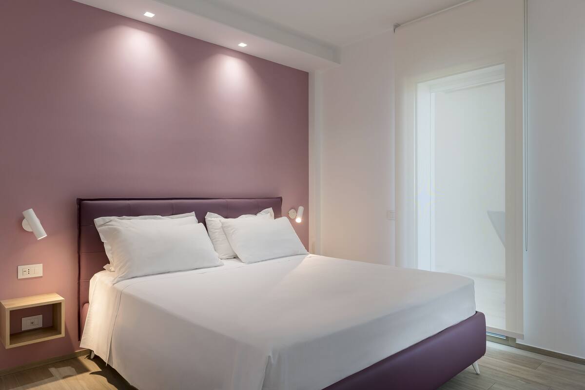 Un dormitorio moderno con una cama grande, una mesita de noche y una lámpara fijada a la pared.