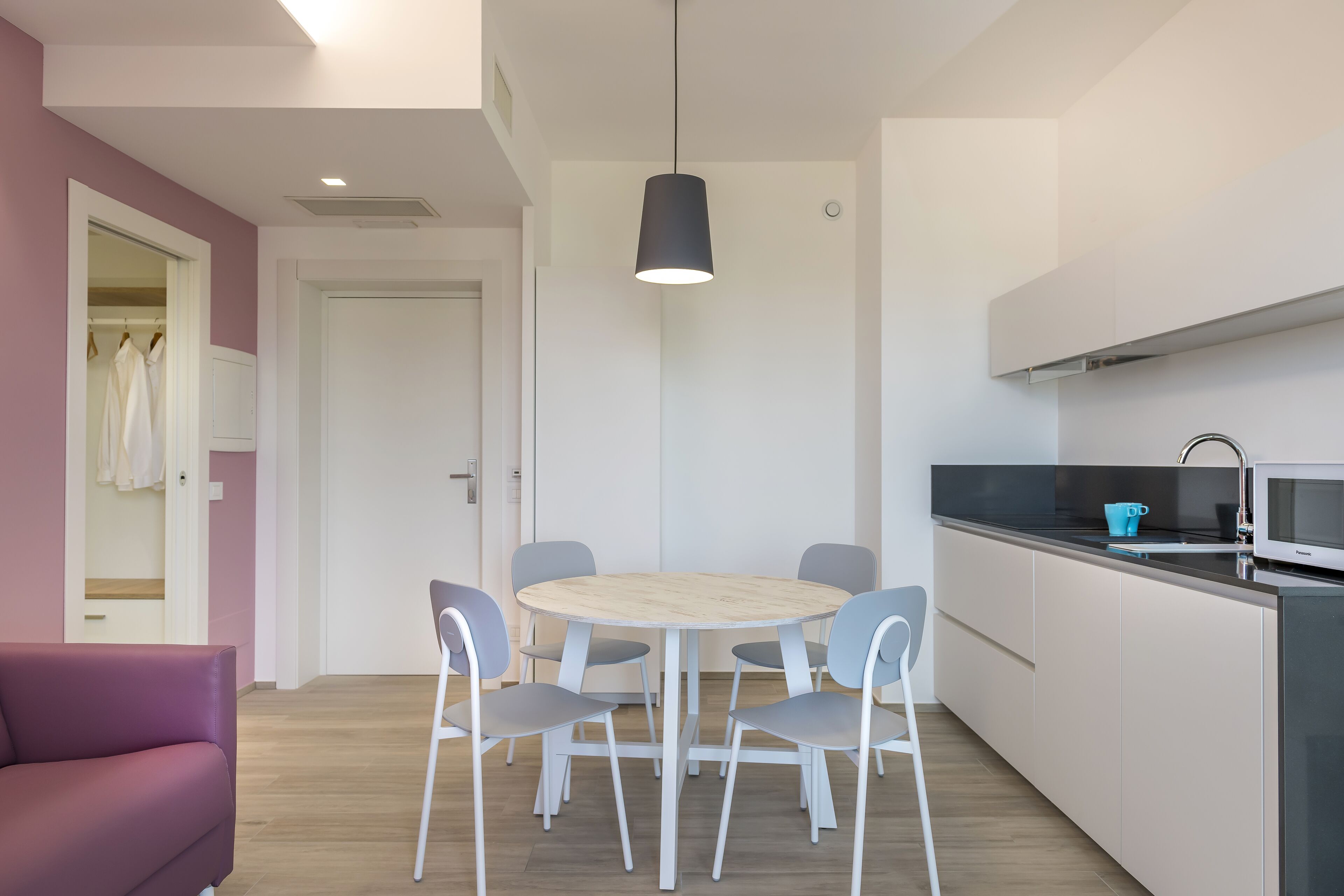 A modern kitchen with a round table and chairs, a hanging light fixture, and a microwave.
