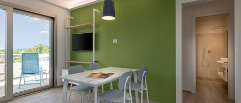 Een moderne kamer met een witte tafel en stoelen, een wandgemonteerde televisie en een groene accentmuur.