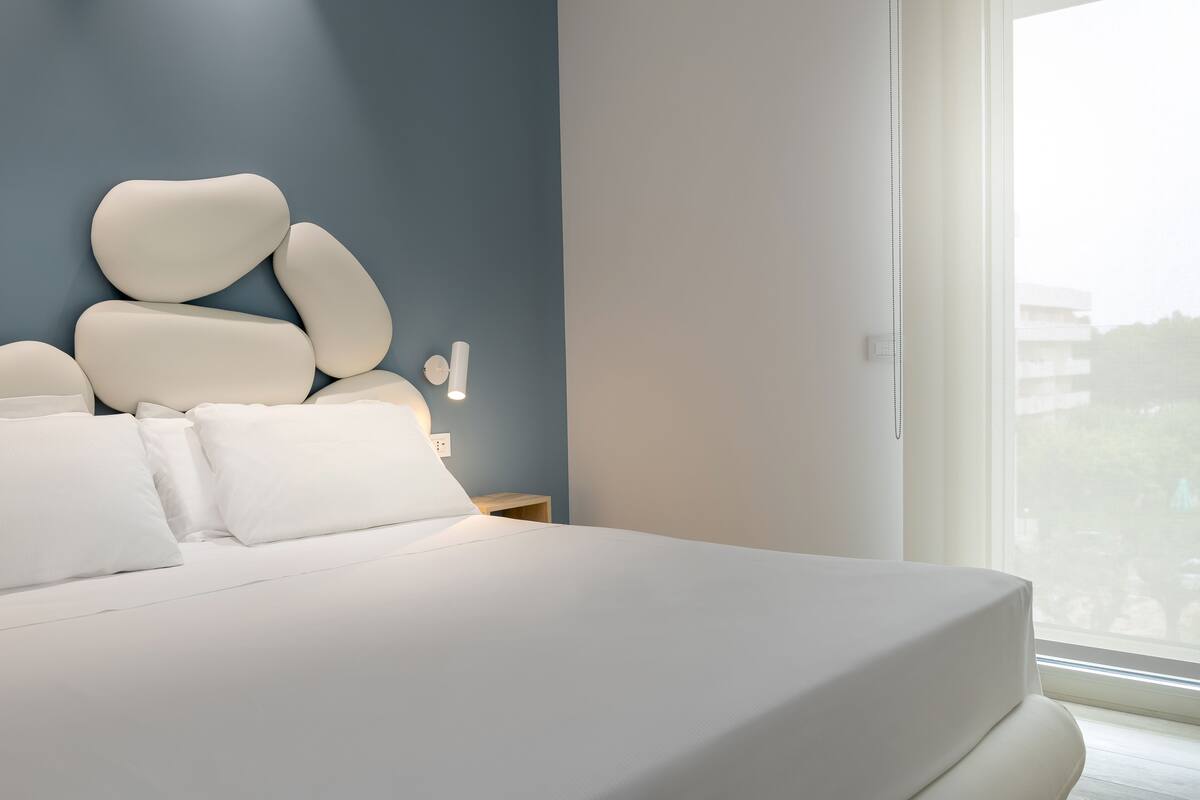 Un dormitorio moderno con una cama grande, una mesita de noche y una lámpara fijada a la pared.