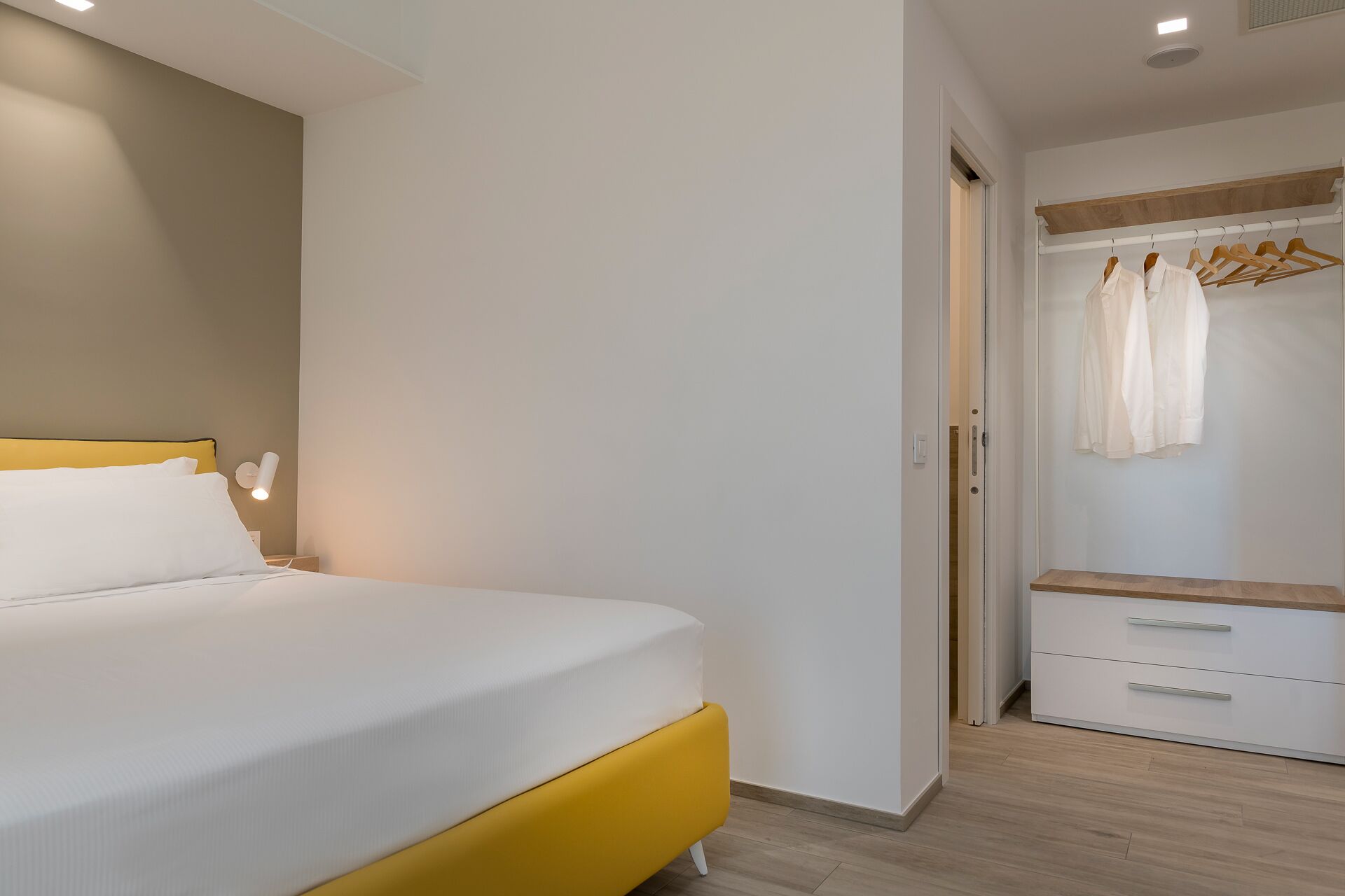 A bedroom with a bed, bedside table, and a wardrobe with hanging clothes.
