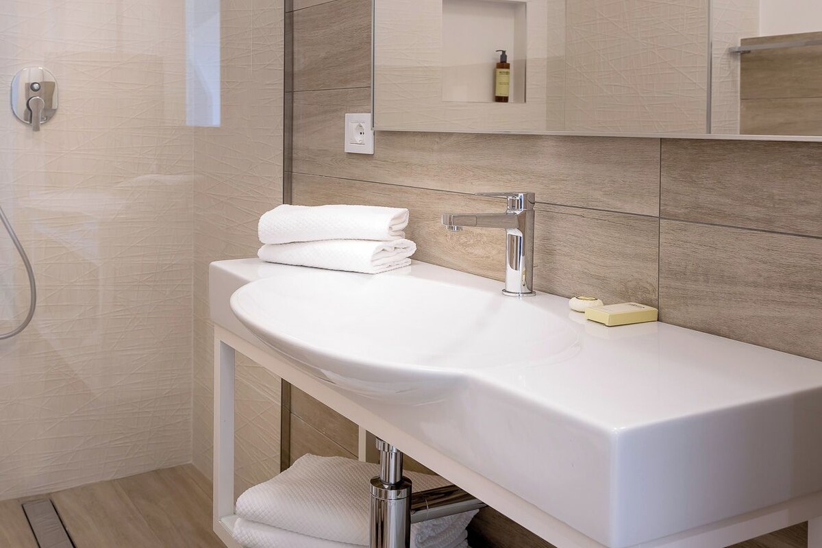 Un bany modern amb un mirall gran, un lavabo blanc i una zona de dutxa.