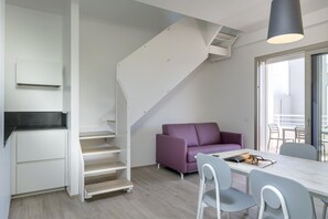 Una cocina moderna con armarios blancos, un sofá púrpura y una zona de comedor con mesa y sillas.