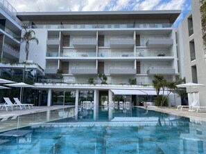 Un edificio moderno de varios pisos con piscina, mobiliario exterior y balcones.