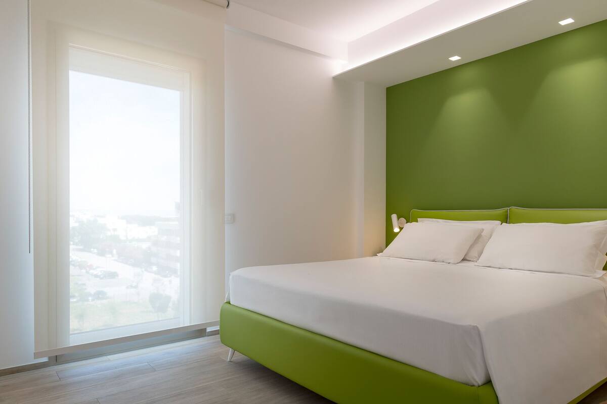 Un dormitorio con cama, pared de acento verde y un ventanal grande.