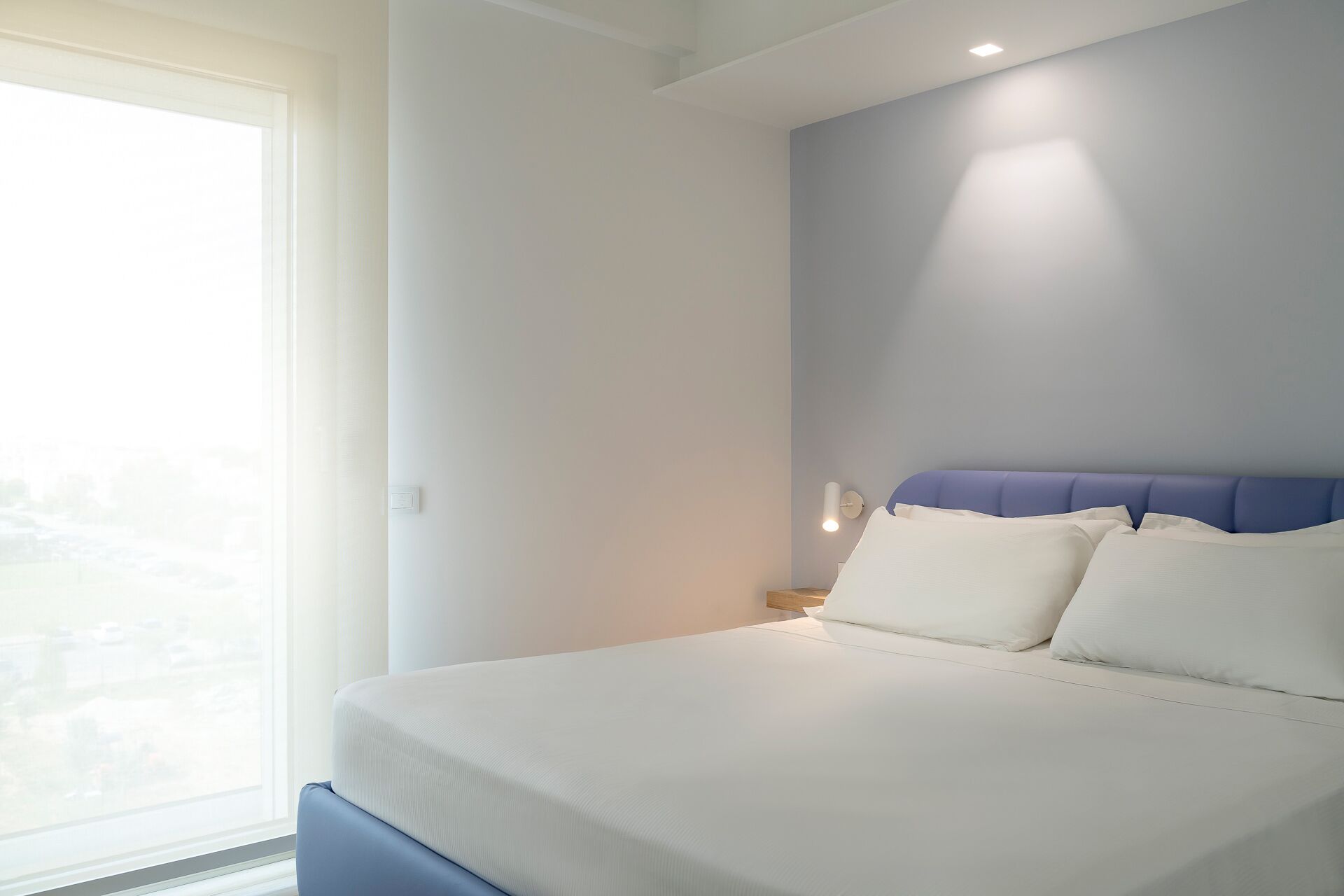 Een moderne slaapkamer met een groot bed, een hoofdeinde en een raam dat voor natuurlijk licht zorgt.