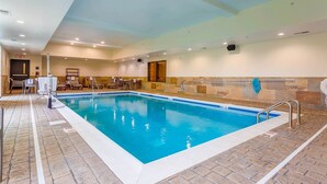 Una piscina interior con agua cristalina, paredes y suelo de baldosas. Hay sillones de descanso y una pequeña mesa cerca de la piscina.