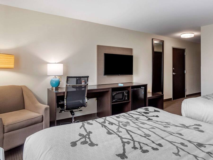 A hotel room with two beds, a desk with a computer, a TV, a lamp, and a chair.