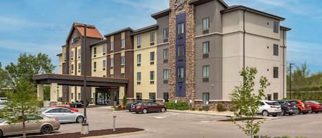 A multi-story hotel with a central entrance, parking lot, and landscaped areas.