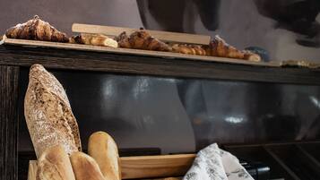 Ein Holzkörbchen mit verschiedenen Brotsorten und einer Blumen-Serviette auf einem Tisch.