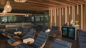 A modern spa area with wooden slatted ceilings, a glass-enclosed hot tub, and lounge chairs with wooden bases. - Hraniční zámeček (Lednice)