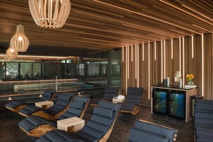 Un área de spa moderna con techos de listones de madera, un jacuzzi con paredes de vidrio y sillones de madera.
