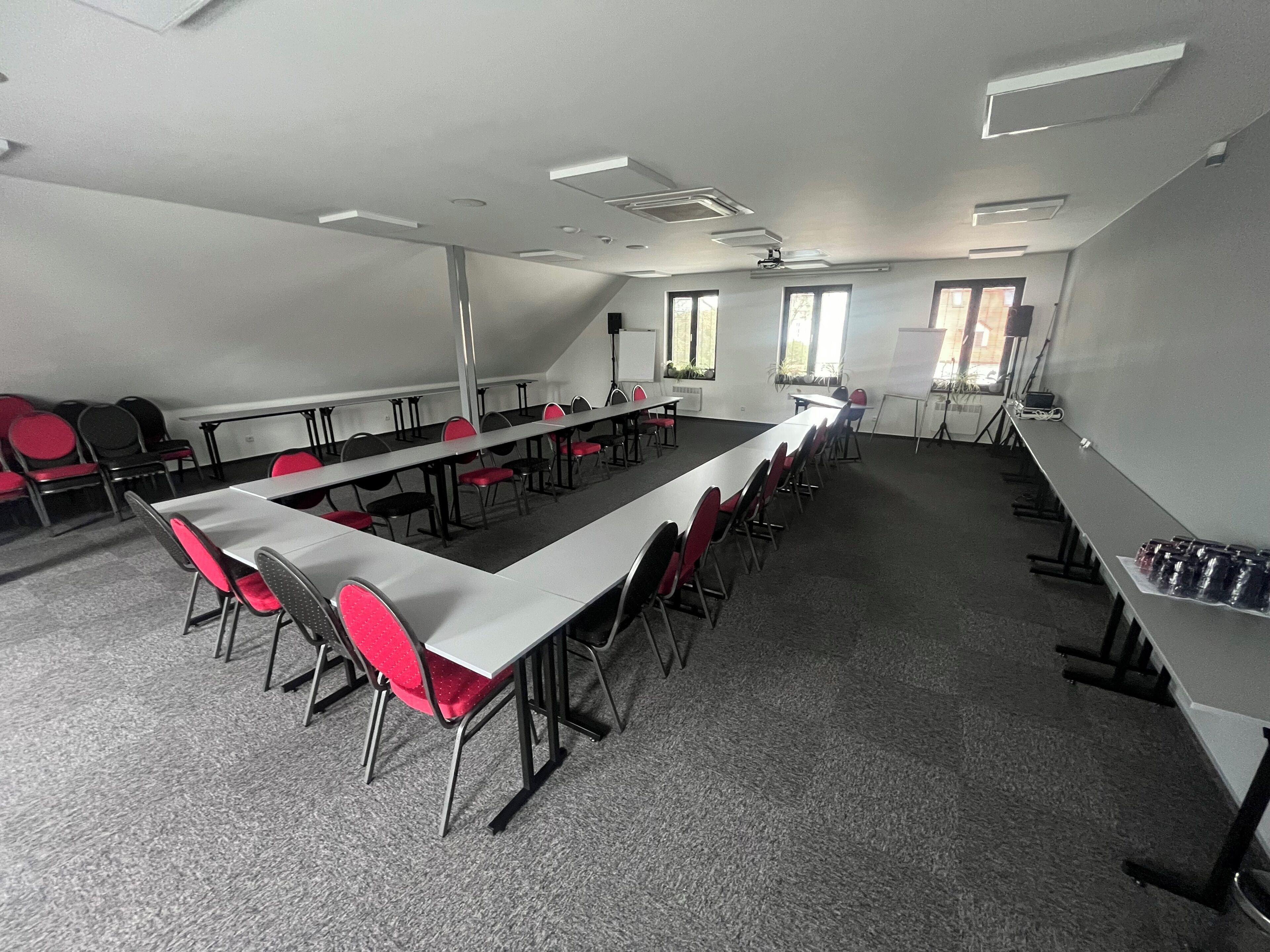 Une salle de conférence avec de longues tables et des chaises, un tableau blanc et des fenêtres.
