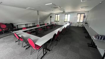 Une salle de conférence avec de longues tables et des chaises, un tableau blanc et des fenêtres.
