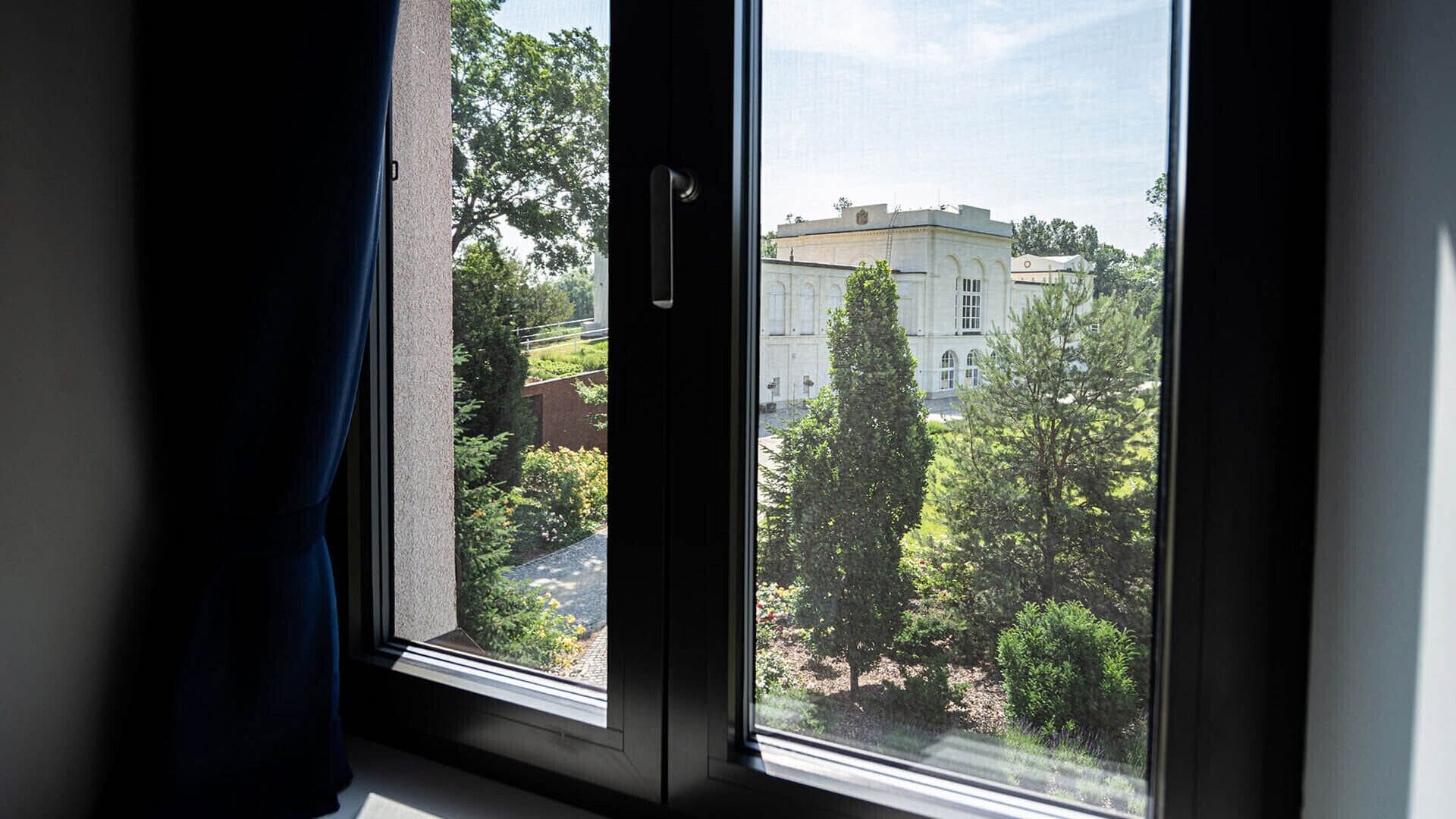 Une fenêtre donnant sur un bâtiment entouré de verdure.