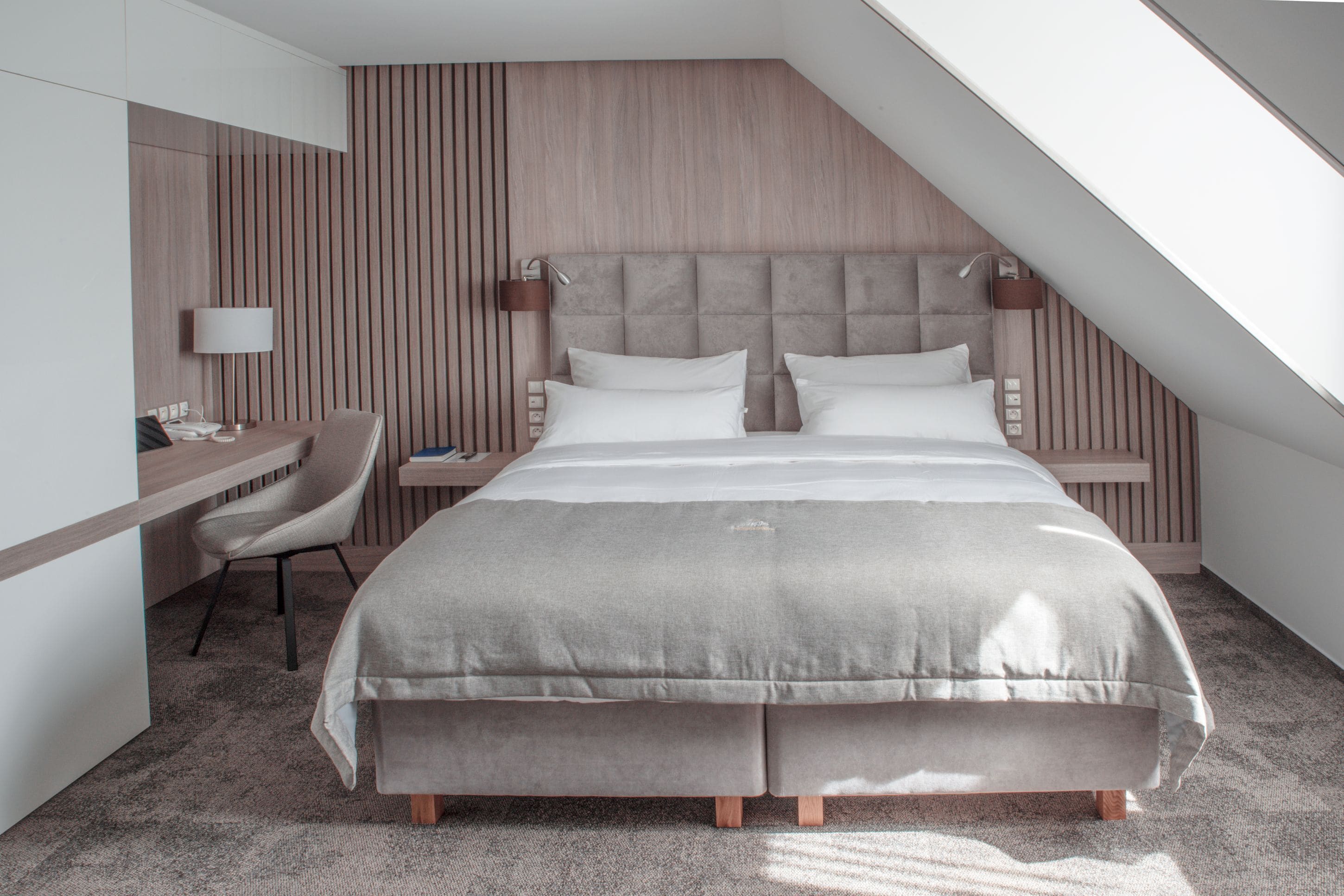 A modern hotel room with a large bed, a desk, and a chair.
