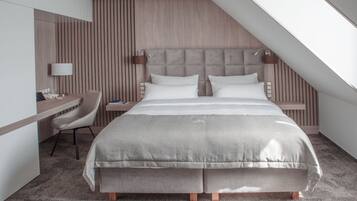 A modern hotel room with a large bed, a desk, and a chair.