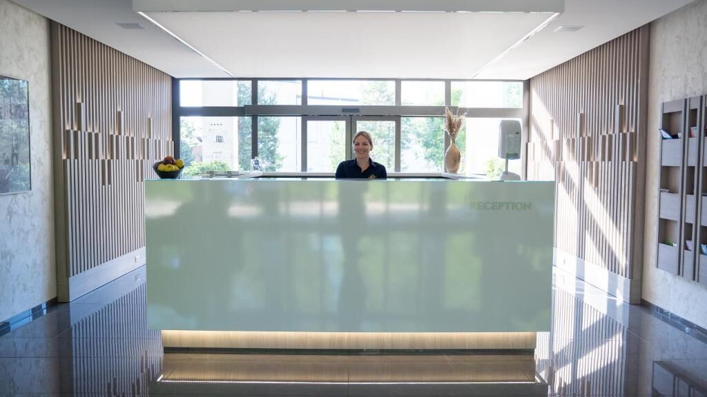 Un área de recepción con diseño moderno, que incluye un mostrador de recepción, un ventanal grande y una pared con listones verticales.